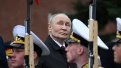 Vladimir Putin observa cómo desfilan los soldados rusos durante un desfile en la Plaza Roja de Moscú. El líder ruso tiene el pelo corto y canoso y lleva una chaqueta negra.