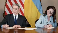 የአሜሪካ ግምጃ ቤት ኃላፊ ስኮት ቤሴንት (በግራ) እና የዩክሬን ምክትል ጠቅላይ ሚኒስትር ዩሊያ ሲቪራይደንኮ (በቀኝ) የተፈጥሮ ሀብት ስምምነቱን ሲፈራረሙ