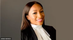 Somtochukwu Maduagu wọ aṣọ dúdù pẹ̀lú aṣọ funfun lábẹ́, tó sì ń rẹ́rìn-ín 