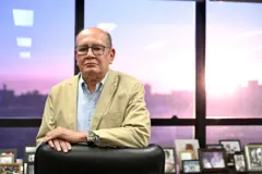 Gilmar Mendes está apoiado em uma cadeira. Atrás dele há vários porta-retratos em uma estante