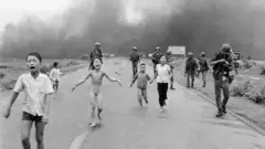 Южновьетнамские войска преследуют испуганных детей, в том числе 9-летнюю Ким Фук (в центре), бегущих по шоссе № 1 недалеко от Транг Банга после авиаудара с применением напалма по предполагаемым укрытиям вьетконговцев, 8 июня 1972 года.