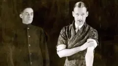 Foto em preto em branco dois homens brancos, um tem bigode pontudo e casaco estampado