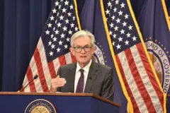 O presidente do Federal Reserve , Jerome Powell, falando num púlpito, com bandeiras dos Estados Unidos ao fundo
