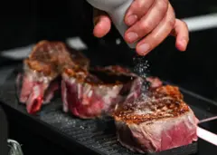 Mão adicionando sal a um pedaço de carne.