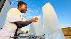 رجل سوداني يصنع مكعبات الثلج لمواجهة حر الطقس.