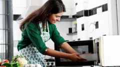 মাইক্রোওয়েভ ওভেনে রান্না করছেন এক নারী 