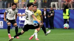 黄色ユニホームのブラジル選手がシュートを放ち、ボールが飛んでいる。近くには白色ユニホームの日本選手2人がいる