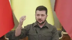 Presidente ucraniano Volodymyr Zelensky falando, de pé.
