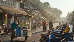 Rua de Luang Prabang, com carrinho tradicional e repleta de motocicletas