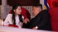 Kim Jong-un e a filha Kim Ju-ae conversando. Eles estão sentados em uma cadeira vermelha.