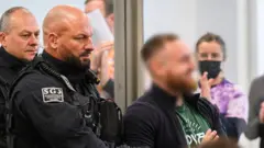 Обвиняемого Йоханна Г. доставляют в зал суда в начале процесса против семи левых экстремистов, обвиняемых в участии в преступной организации, 25 ноября 2025 года