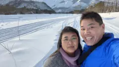Casal sorrindo para selfie em área aberta com neve