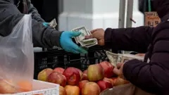 متسوق يحمل أوراقاً نقدية أمريكية أثناء دفع ثمن المنتجات في سوق المزارعين في سان فرانسيسكو، كاليفورنيا، الولايات المتحدة، يوم الخميس، 27 مارس/آذار 2025.