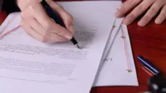 Foto de uma pessoa assinando um documento.