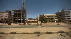 تُظهر الصورة أحد الشوارع الرئيسية في مدينة أم درمان، وقد خلت تمامًا من السيارات والمارّة، بينما أُغلقت المحالّ التجارية وتراكم الغبار والحطام على الأرصفة