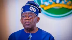 Shugaba Bola Tinubu sanye da shuɗiyar kaftani da shudiyar hula da farin gilashi a fuskarsa