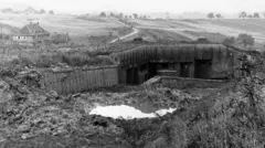 Bunker destruído da Segunda Guerra Mundial, em um campo aberto com um casarão ao fundo