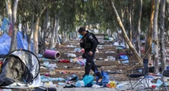 Um agente de segurança caminha entre tendas de acampamento e escombros