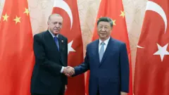 Cumhurbaşkanı Erdoğan Çin Devlet Başkanı Şi Cinping ile iki ülke bayrakları önünde el sıkışarak poz veriyor