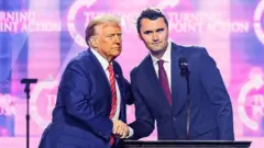 Donald Trump y CHarlie Kirk se dan la mano en un escenario.