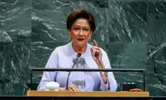 A primeira-ministra de Trinidad e Tobago, Kamla Persad-Bissessar, está de pé em um púlpito e levanta uma das mãos enquanto fala.