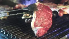 Carne sendo virada enquanto assaroleta de números de 1 a 100churrasqueira