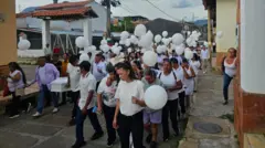 Un grupo de niños y niñas con camisetas blancas y globos blancos.