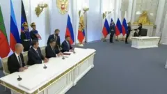The four Russian-appointed leaders sign also, on a desk set away from Putin