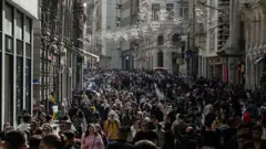 أشخاص يسيرون في أحد شوارع إسطنبول المكتظ، وتزين الشارع زينة عيد الميلاد.
