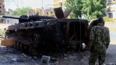 أحد المقاتلين يقف أمام مركبة عسكرية محترقة في شمال الخرطوم
