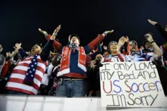 Torcedores dos Estados Unidos incentivam sua equipe, com camisas, faixas e cachecóis com as cores da bandeira americana, durante um jogo noturno