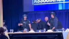 Perezida Donald Trump atwawe n'abashinzwe umutekano agenda yunamye, mu gihe abandi bamwe bahagaze, inyuma hari gitambaro kinini cy'ubururu.