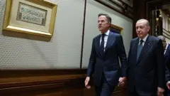 Erdoğan ve Rutte el ele duvarda Arapça yazıların olduğu bir koridorda yürüyor.
