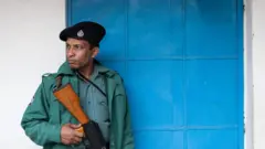 বন্দুক হাতে পুলিশের একজন সদস্য দাঁড়িয়ে আছেন