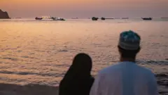 在霍爾木茲海峽附近的阿曼馬斯開特港，一對當地男女在海灘上眺望滯留港口的國際船舶（18/6/2026）