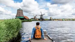 Hombre sentado en el muelle mirando los molinos de viento en Zaanse Schans, Zaandam, Países Bajos.