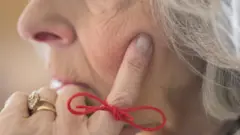 Una mujer anciana que padece alzhémier con un cordel anudado en su dedo como recordatoreio de algo
