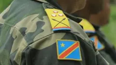 Umusirikare utagaragara mu maso wambaye impuzankano y'ingabo za Repubulika ya Demokarasi ya Congo, igaragaza ipeti rya Kapiteni riri ku rutugu, mu mabara y'ibendera ry'icyo gihugu y'icyatsi kibisi, umuhondo n'umutuku. 