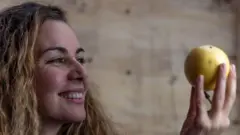 Mulher segura um maracujá e olha para a fruta sorrindo