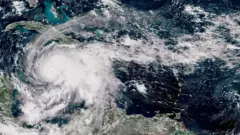 Satelitski snimak prikazuje veliki, dobro definisan uragan iznad Karipskog mora. Oluja ima jasno oko i spiralne oblačne trake koje se protežu preko Haitija, Dominikanske Republike i istočne Kube, sa okolnim oblačnim pokrivačem koji se proteže prema Bahamima i severnim delovima Južne Amerike