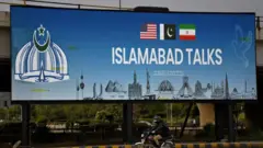 「ISLAMABAD TALKS」と大きく書かれた看板の前を、バイクに乗った人が通過している

