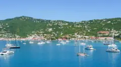 مراكب بيضاء على صفحة مياه زرقاء، في حضن تلال خضراء مرصّعة بمبانٍ بيضاء اللون، في جزيرة سانت توماس