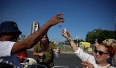 Grupo com copos nas mãos comemora libertação dos reféns, em dia ensolarado