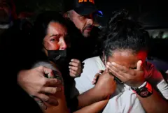 Un hombre abraza a dos mujeres que están desconsoladas llorando mientras intenta sacarlas de donde están.