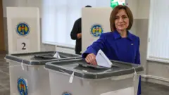 Майя Санду в синем костюме опускает бюллетень в урну на избирательном участке.