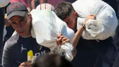 Двое мужчин несут на спине мешки (24 июля 2025 года)