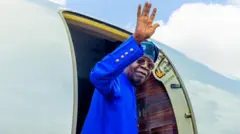 Aarẹ Tinubu n juwọ lẹnu ọna baluu kan.