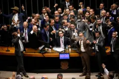 Hugo Motta sentado à Mesa Diretora, cercado por dezenas de parlamentares