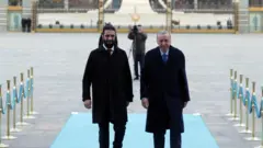 Erdoğan sağda, Şara solda, ikisi de siyah paltolu mavi bir halıda yürüyorlar, arkada bir fotoğrafçının flu görüntüsü var.