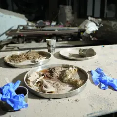Pratos com comida sobre uma mesa coberta de pó branco espesso, com um par de luvas de látex de médico em cada lado - como se tivessem sido jogadas fora por uma pessoa no momento em que o avião atingiu o prédio